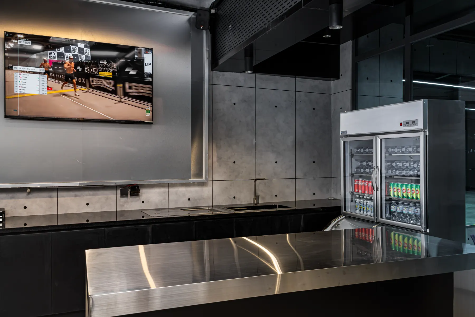 Khu lounge tại HYPE — quầy bar inox, màn hình và tủ đồ uống