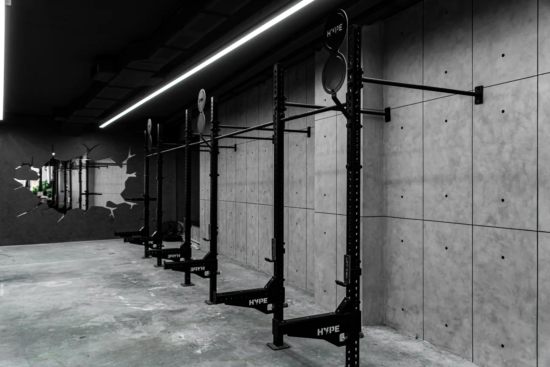 Khu Strength tại HYPE — giàn tạ chạy dọc tường bê tông dưới đèn LED
